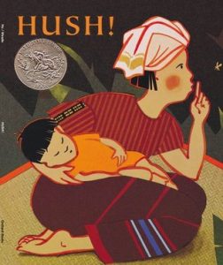 On the book cover of Hush by Monfong Ho a woman holds a child as she shushes with her finger