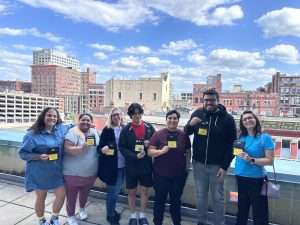 IDEA Public Schools teachers smiling at the camera and showing their AP Reading badges in front of the Cincinnati, Ohio skyline